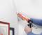 Osoba uszczelnia spoina w rogu dwóch ścian za pomocą pistoletu do silikonu. Malowanie w tle.