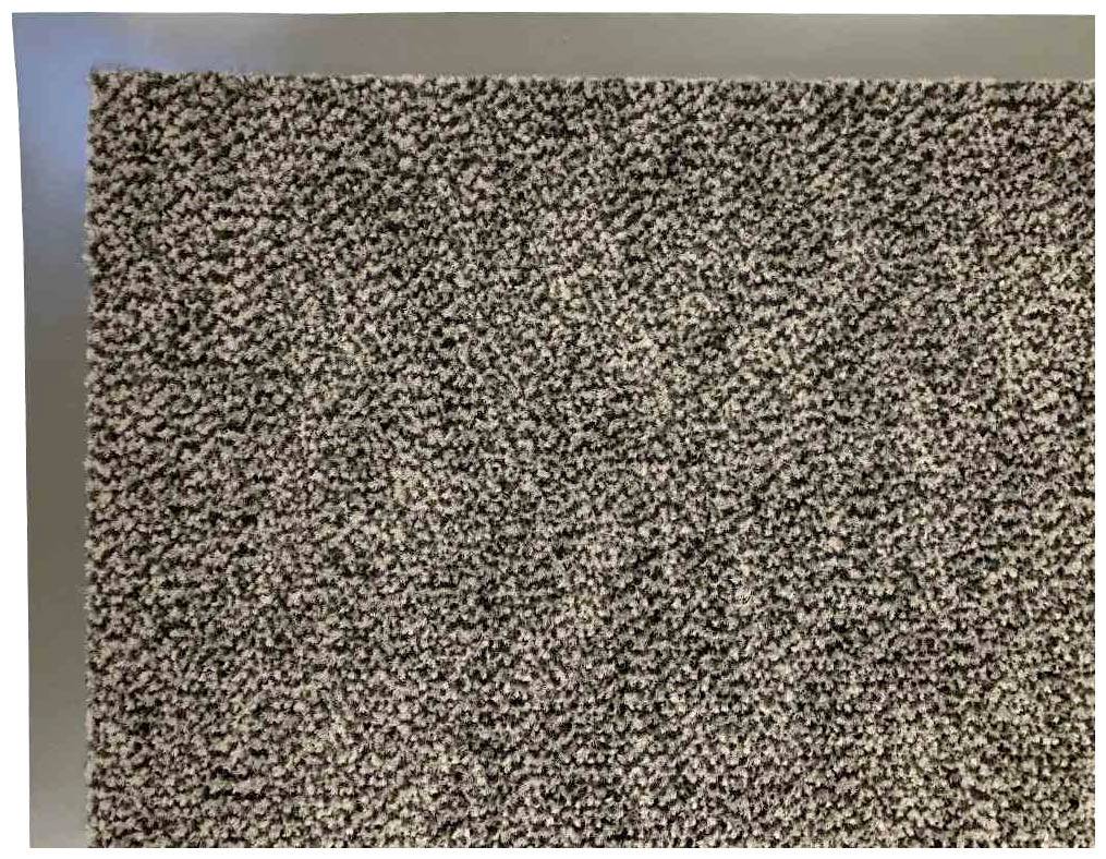 Szary, grubo strukturyzowany dywan w zbliżeniu. Dywan posiada jednolitą, ziarnistą powierzchnię z mieszanymi odcieniami szarości.