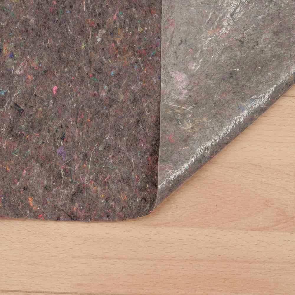 Szara filcowa podkładka leży częściowo na przezroczystej folii plastikowej, która spoczywa na drewnianej podłodze.