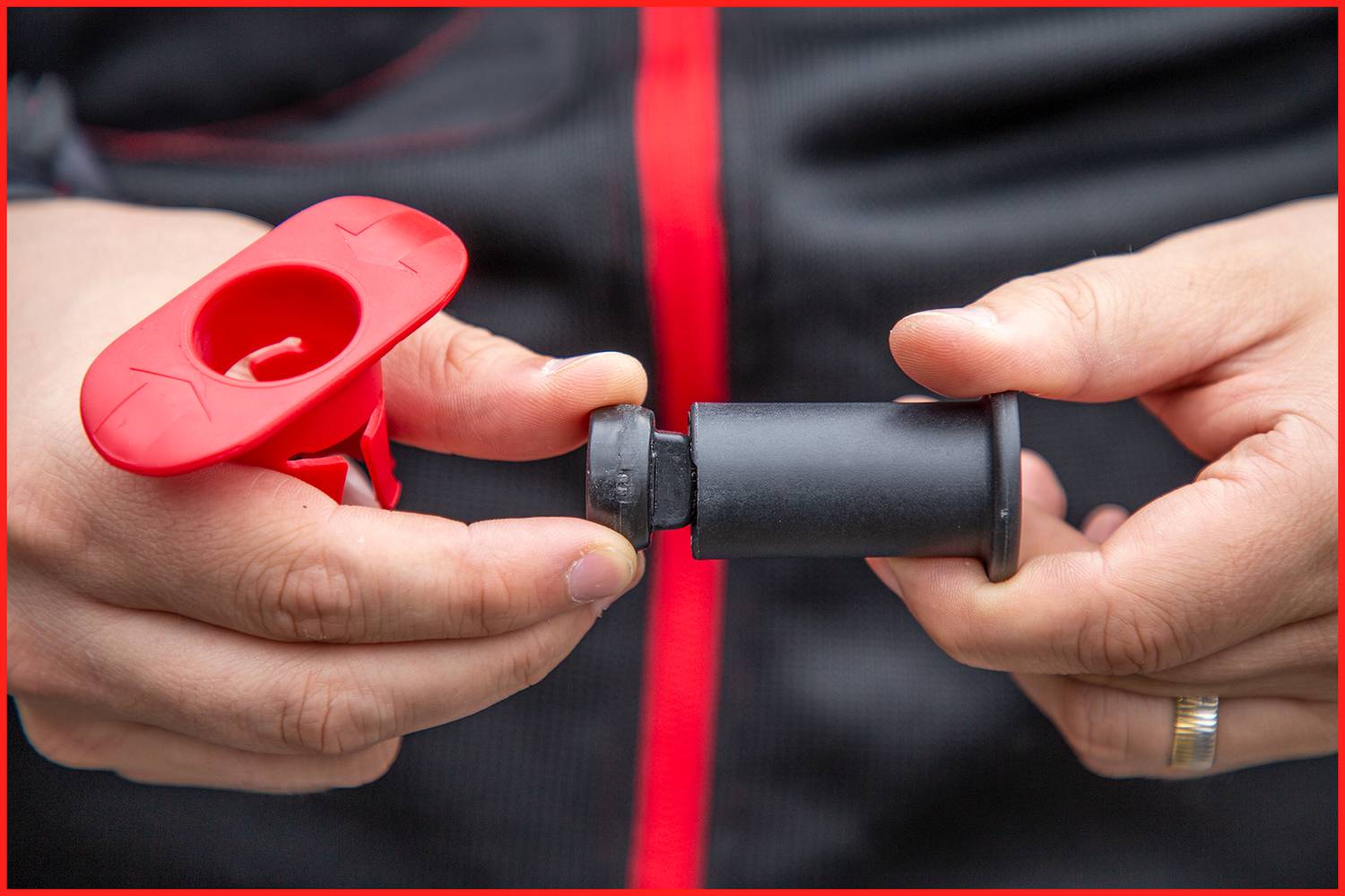 Osoba trzyma czerwoną plastikową dyszę i czarny korek, które do siebie pasują. Tło rozmyte. W kontekście prawdopodobnie do instrukcji montażowej.