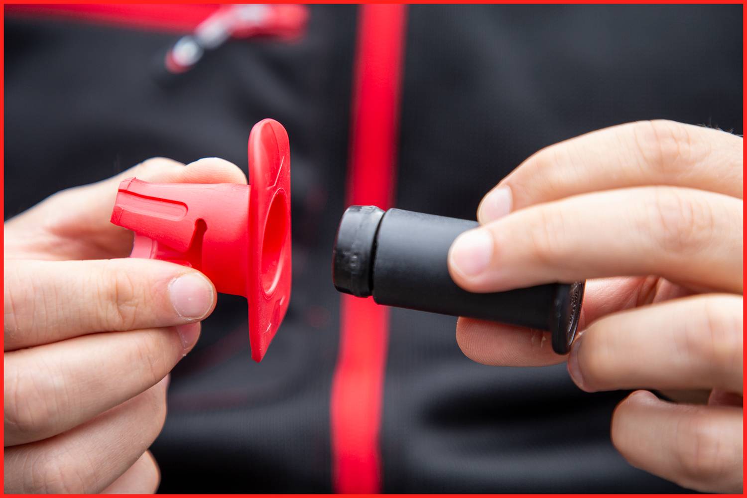 Dwie ręce trzymają czarny i czerwony element z tworzywa sztucznego, prawdopodobnie część lub narzędzie, na ciemnym tle.