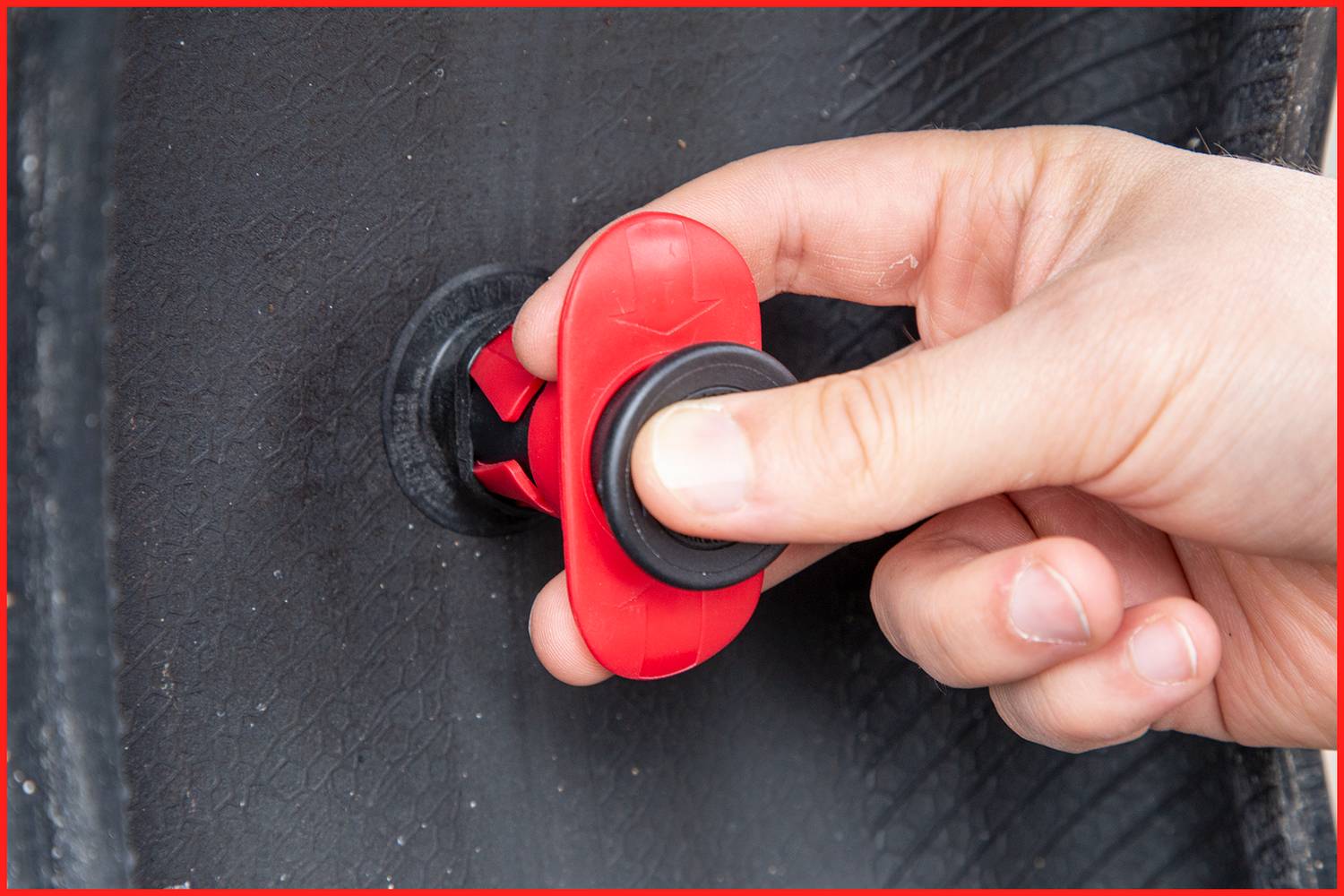 Zbliżenie dłoni obracającej czerwony zawór na oponie.