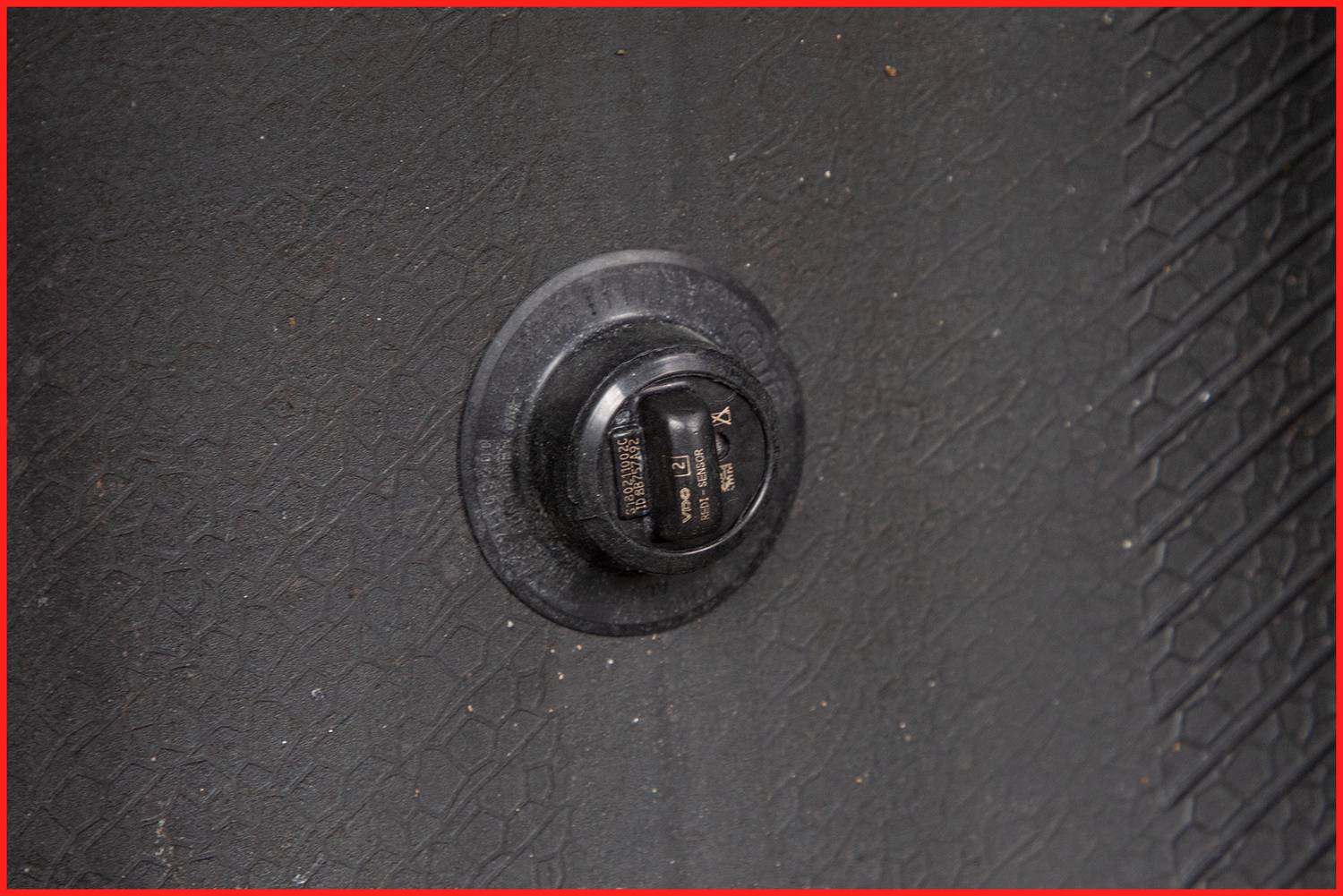 Zbliżenie zaworu na oponie samochodu; czarny zawór na czarnej powierzchni z delikatnym wzorem.