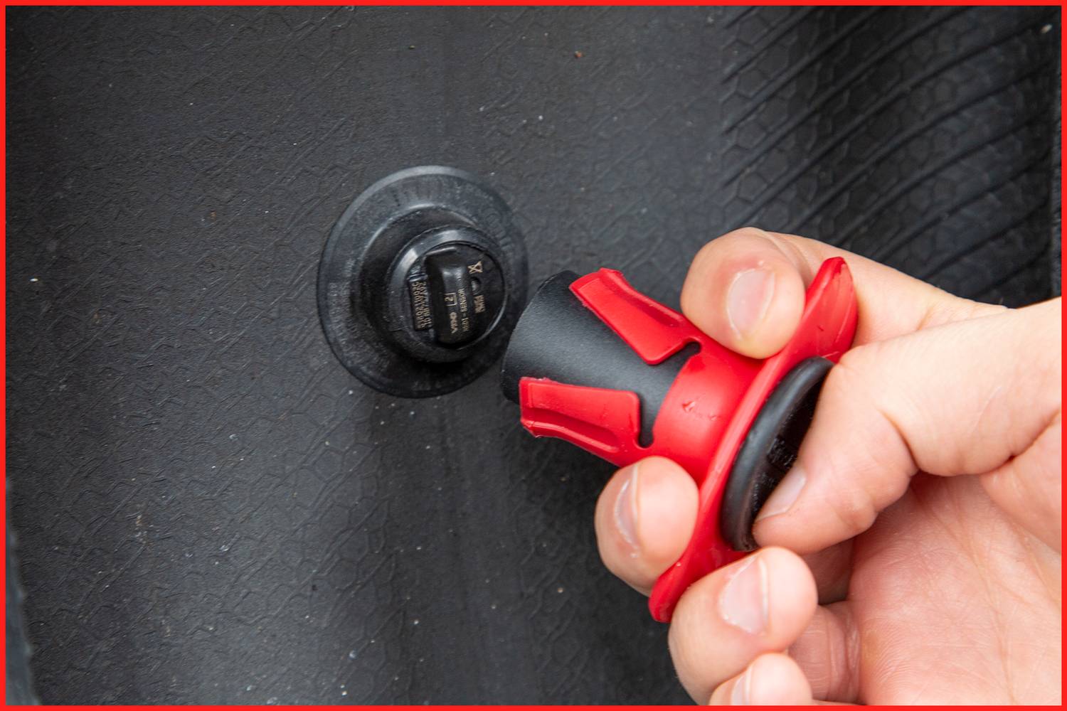 Ręka odkręca czarny korek z czerwonym uchwytem z zaworu na czarnym podłożu.