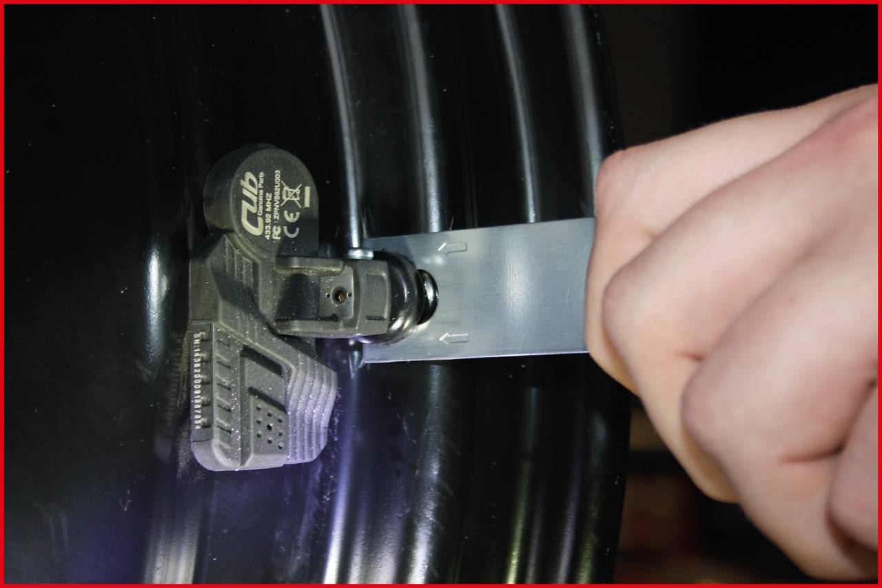 Zbliżenie dłoni napinającej metalową opaskę wokół czarnego cylindra. Do opaski przymocowany jest czujnik.