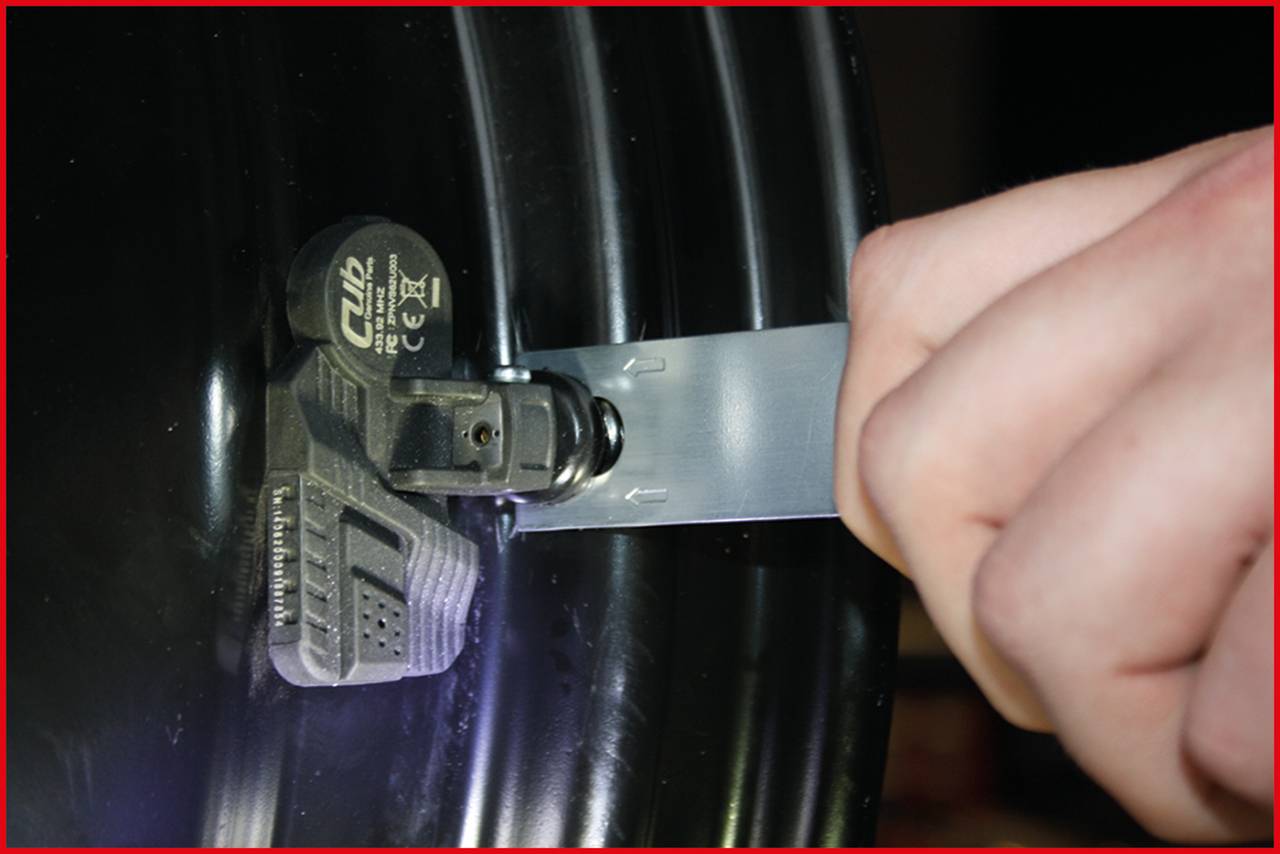 Metalowa opaska zostaje nałożona na czarne urządzenie zamocowane na obręczy koła.