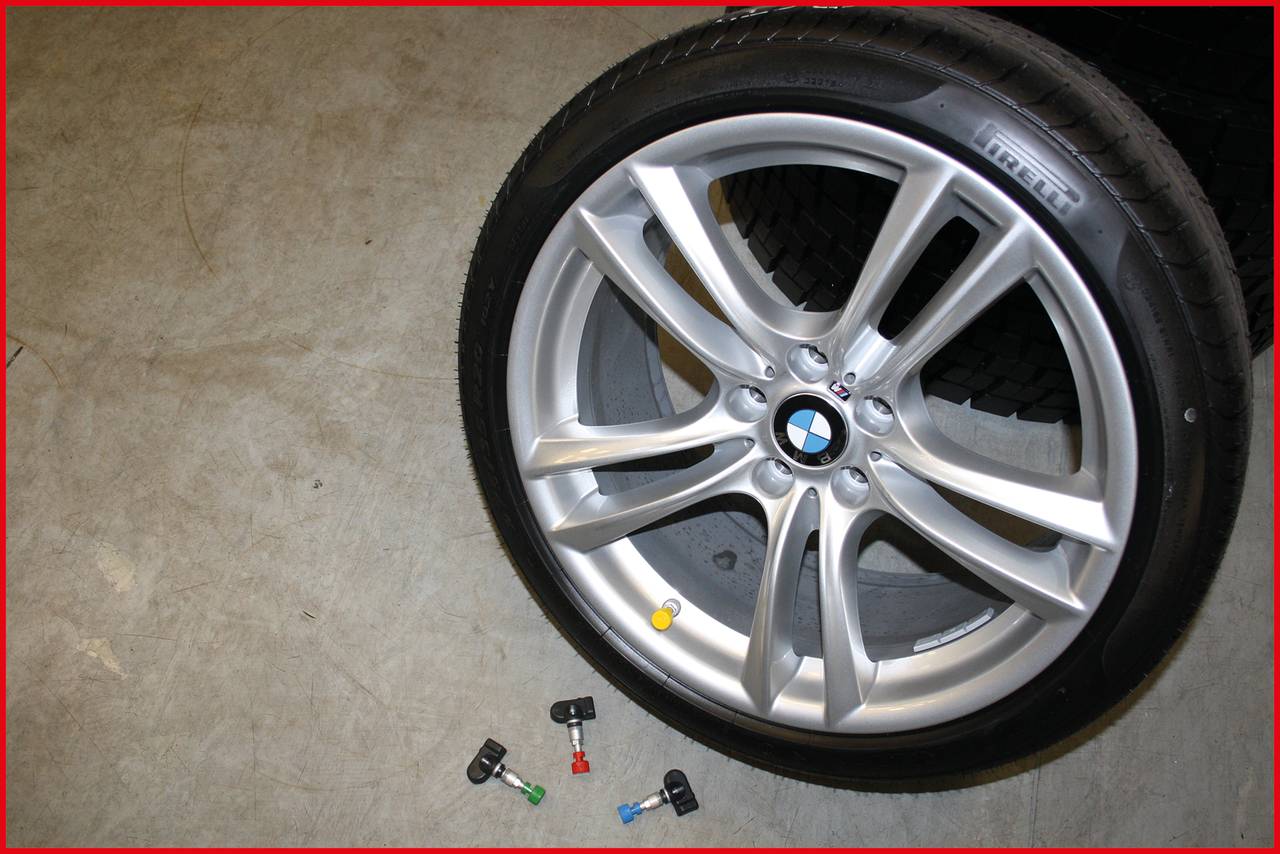 Srebrne kółko felgi samochodowej z logo BMW leży na podłodze. Obok niego znajdują się małe kolorowe obiekty.