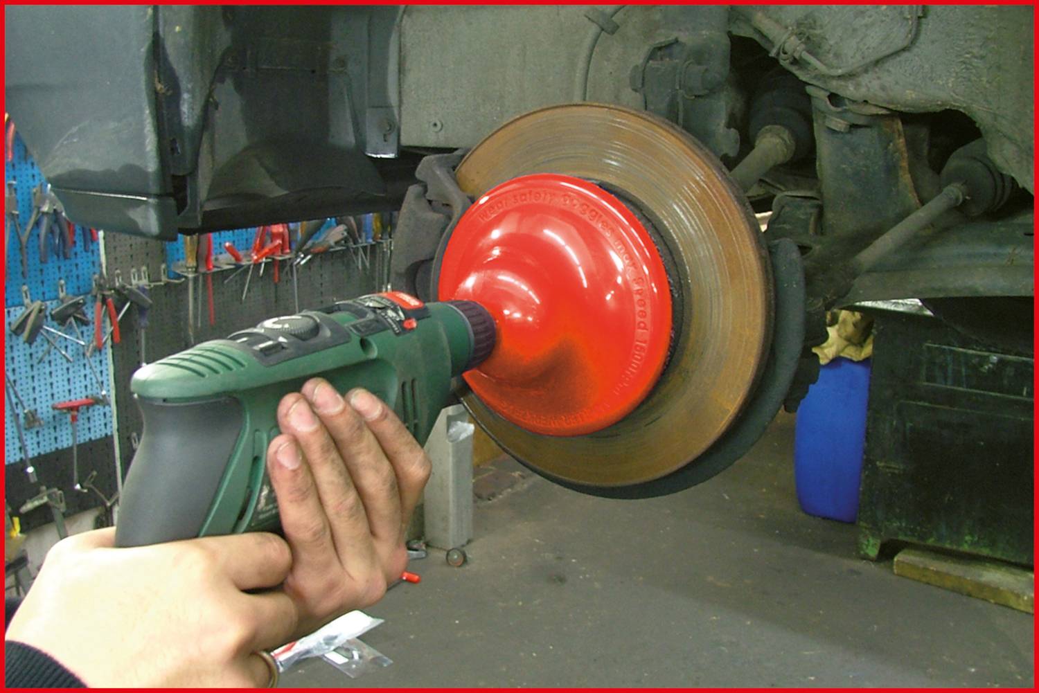 Osoba czyści tarczę hamulcową samochodu za pomocą adaptera do wiertarki w warsztacie. W tle widoczne są narzędzia.