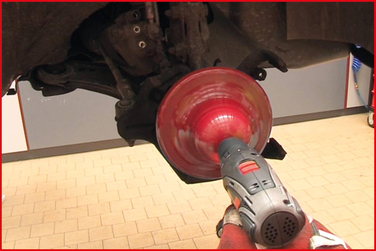 Zbliżenie samochodu naprawianego w warsztacie. Mechanik poleruje obracającą się tarczę hamulcową za pomocą specjalistycznego urządzenia.