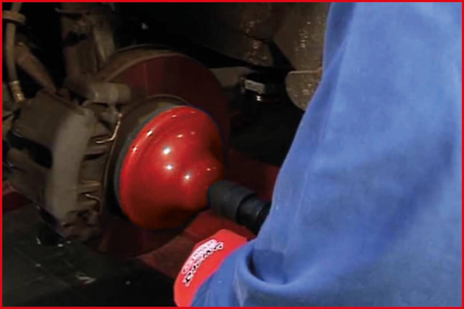 Osoba pracuje przy oponie samochodu za pomocą elektronarzędzia. Koncentracja skupiona jest na procesie obracania koła.