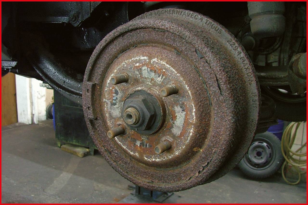 Zardzewiała tarcza hamulcowa starego pojazdu zamontowana na podnośniku warsztatowym.