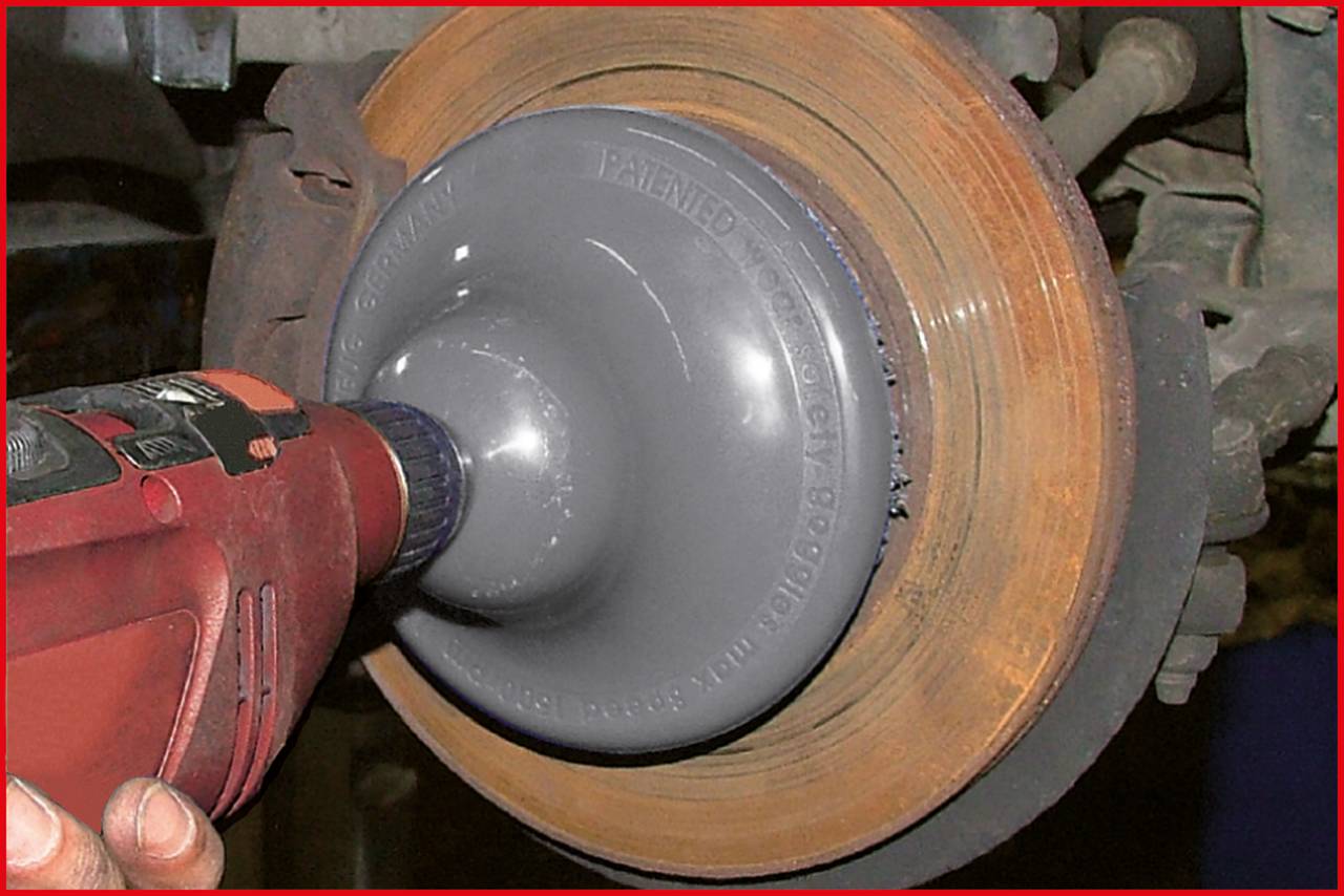 Obrotowa tarcza szlifierska zamocowana na wiertarce jest używana do czyszczenia zardzewiałej tarczy hamulcowej.