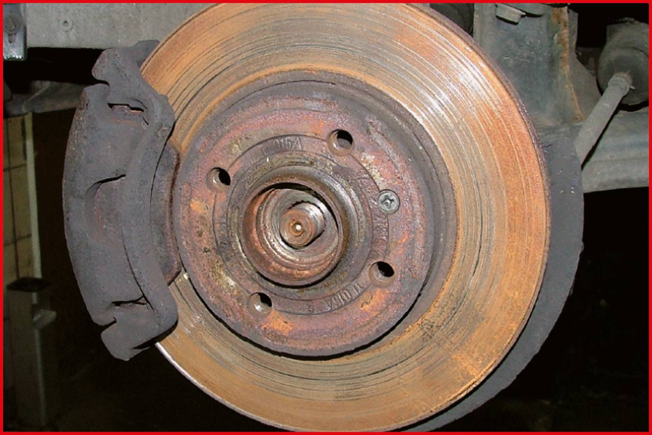 Zbliżenie zardzewiałej tarczy hamulcowej z klockami hamulcowymi na pojeździe.