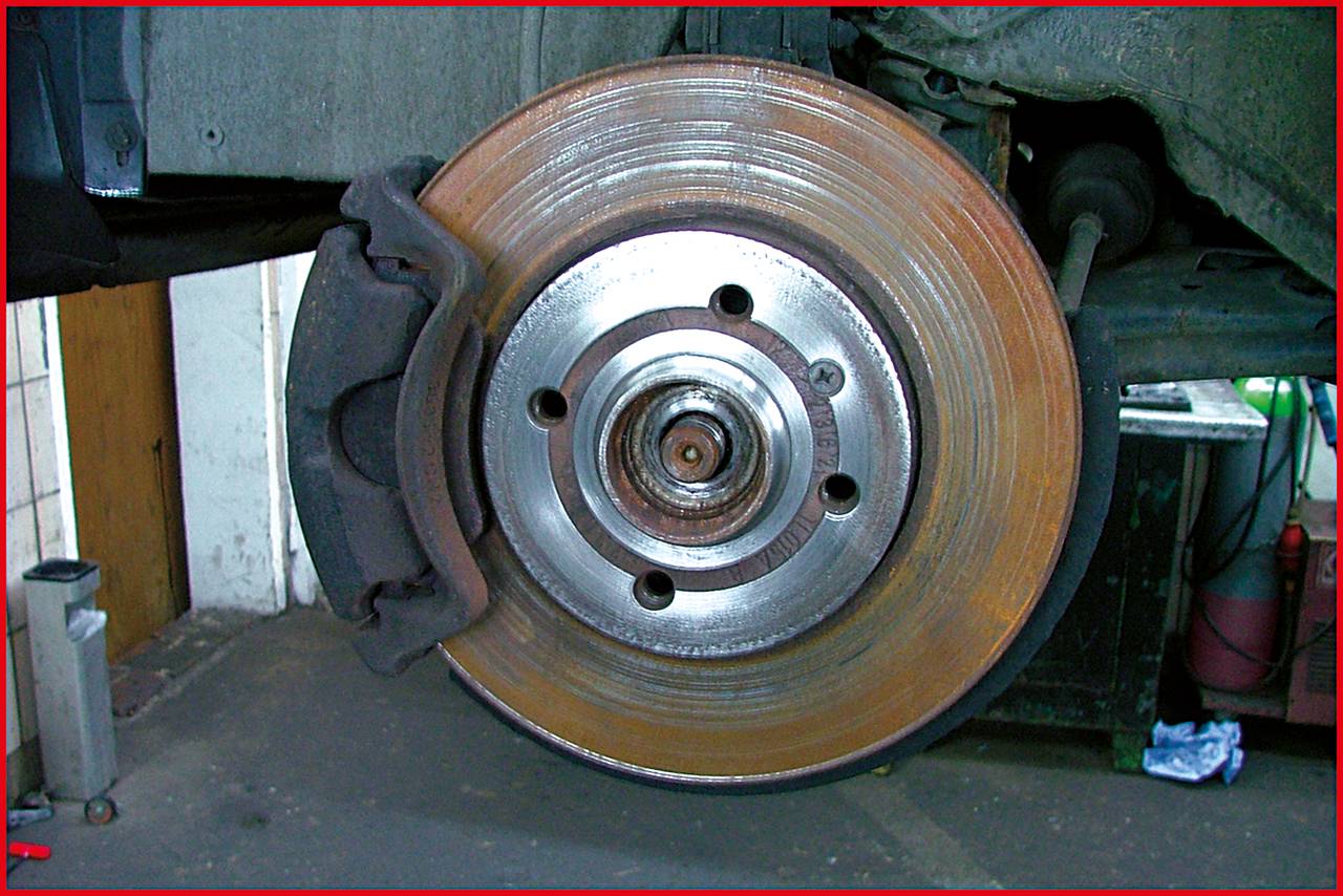 Zużyta tarcza hamulcowa pojazdu w środowisku warsztatu, ukazująca korozję i ślady eksploatacji.