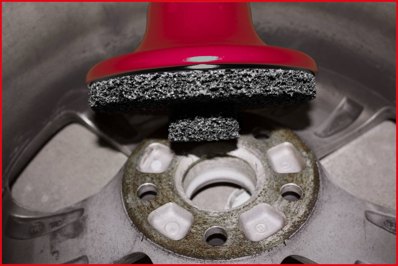 Szczotka czyści felgę samochodu, koncentrując się na korozji lub zabrudzeniach wokół piasty koła.