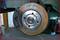 Tarcza hamulcowa samochodu z widoczną klocką hamulcową w środowisku warsztatu samochodowego.