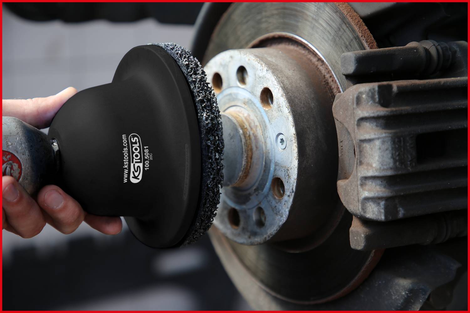 Ręka trzyma narzędzie do szlifowania lub czyszczenia tarczy hamulcowej pojazdu. Narzędzie posiada uchwyt i czarną powierzchnię.