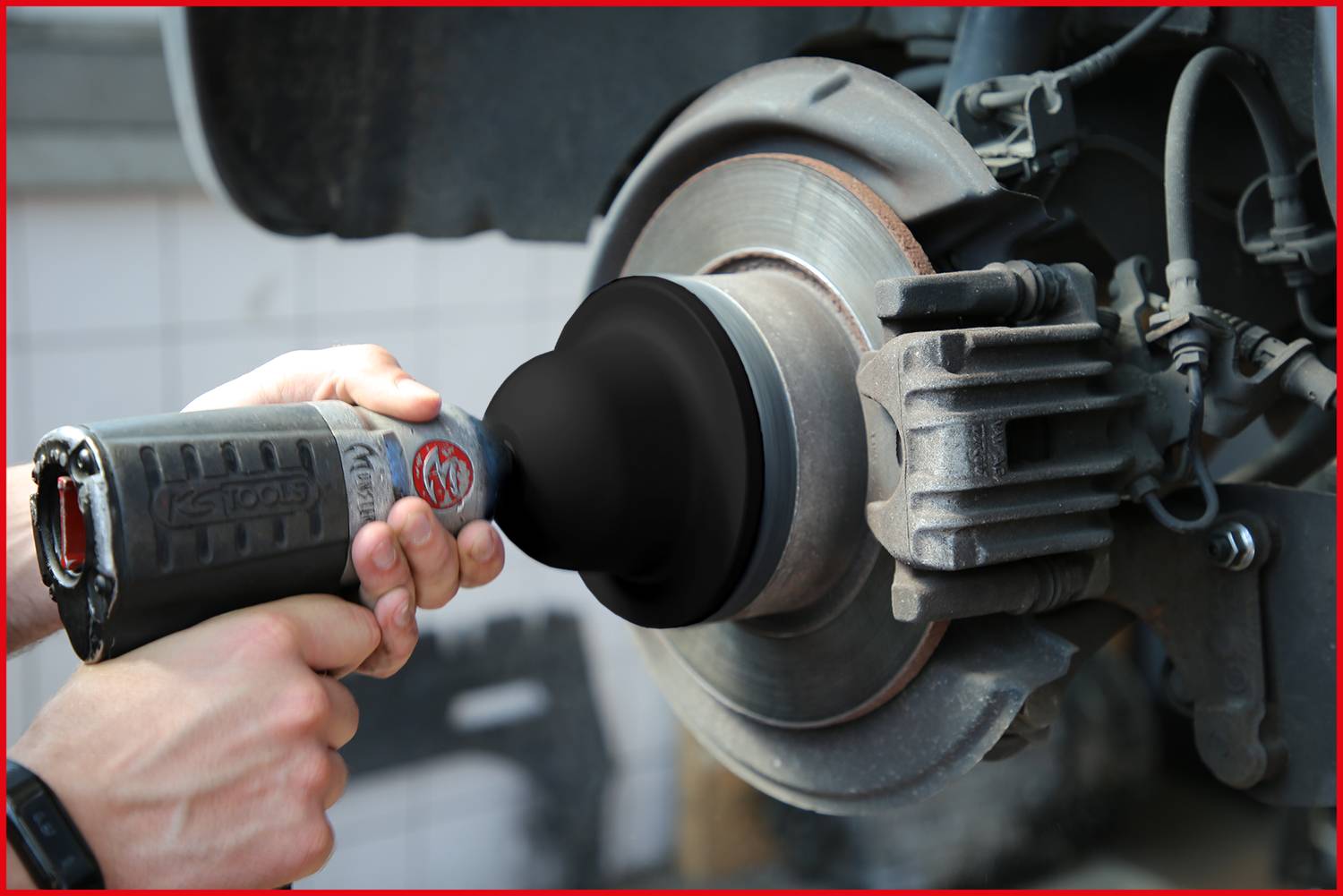 Osoba czyści tarczę hamulcową za pomocą elektronarzędzia. Tarcza hamulcowa jest srebrna i jest polerowana.