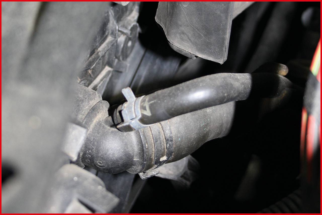 Czarny wąż gumowy w kontekście mechanicznym lub samochodowym, otoczony metalowymi częściami i przewodami.