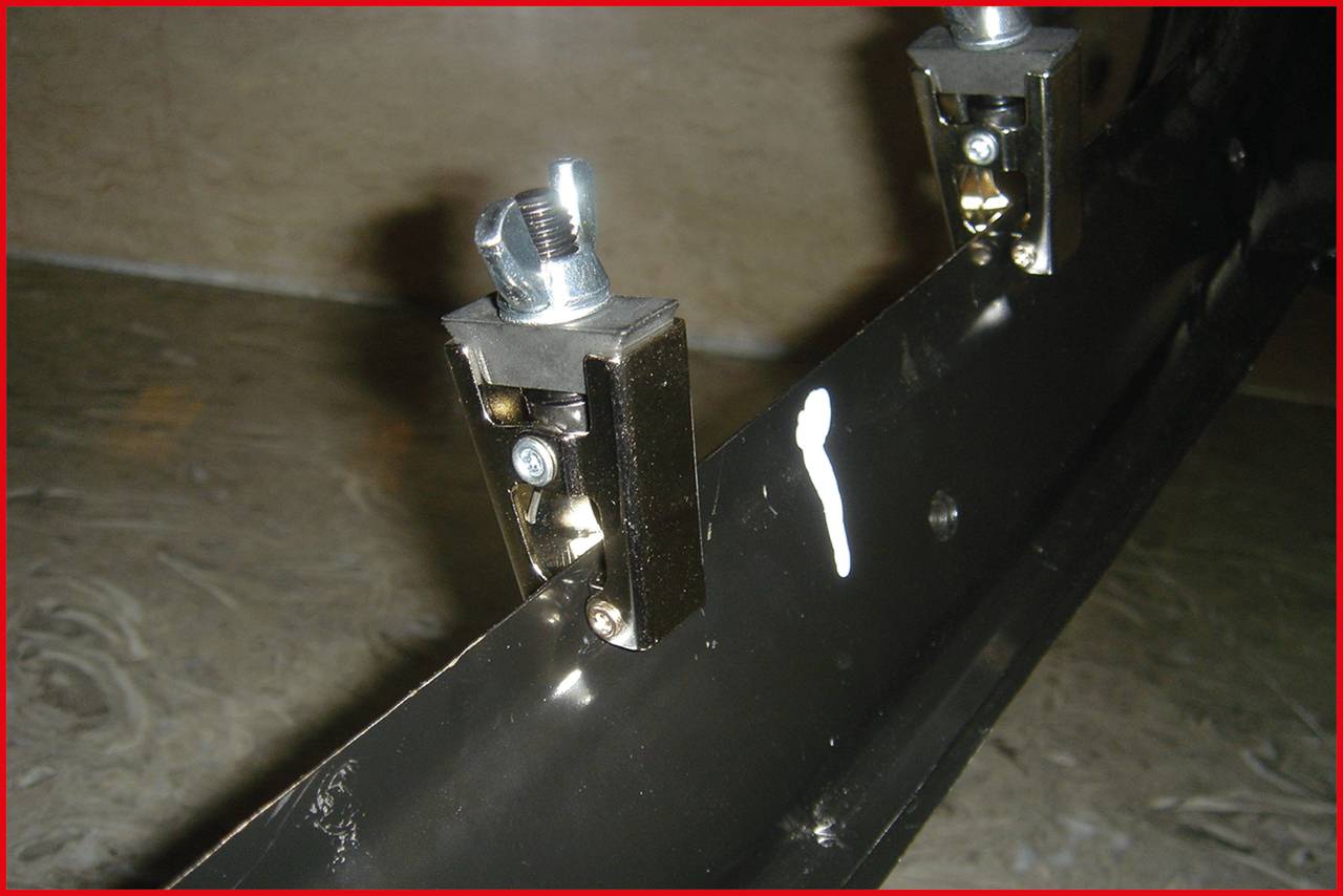 Zbliżenie czarnego elementu metalowego z srebrnymi zamknięciami śrubowymi. Jeden element jest oznaczony białą plamką farby.