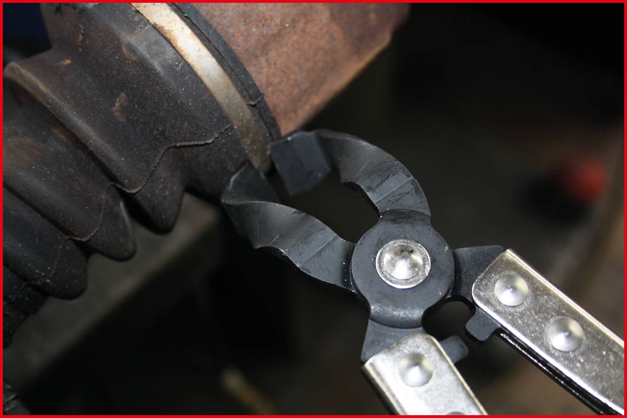 Szczypce przecinają czarny kabel biegnący przez zardzewiałą metalową rurę.