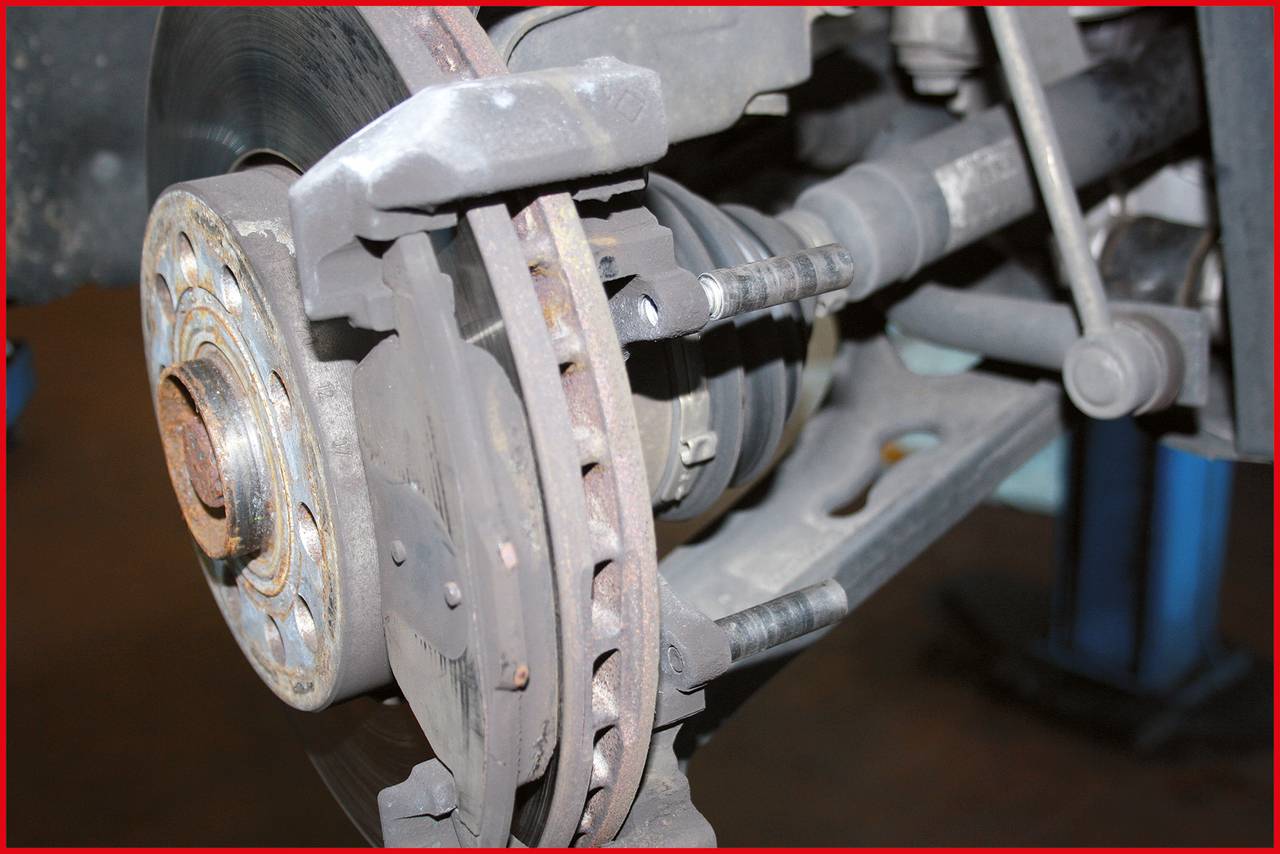 Zbliżenie mechanizmu hamulcowego samochodu z tarczą hamulcową i klockami hamulcowymi. Prezentuje szczegóły zużycia i komponenty techniczne.