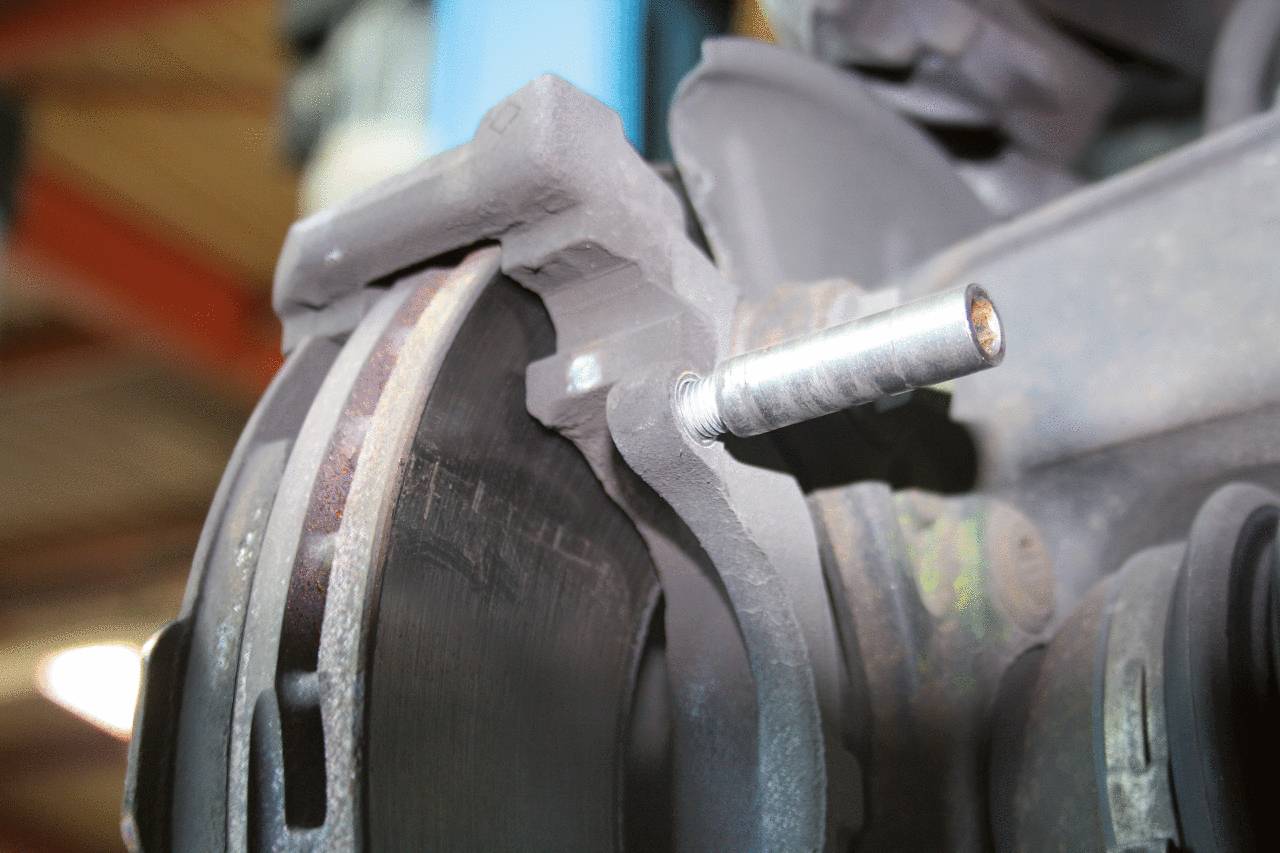 Zbliżenie zużytego układu hamulcowego samochodu w warsztacie, wskazujące na rutynową kontrolę lub serwis.