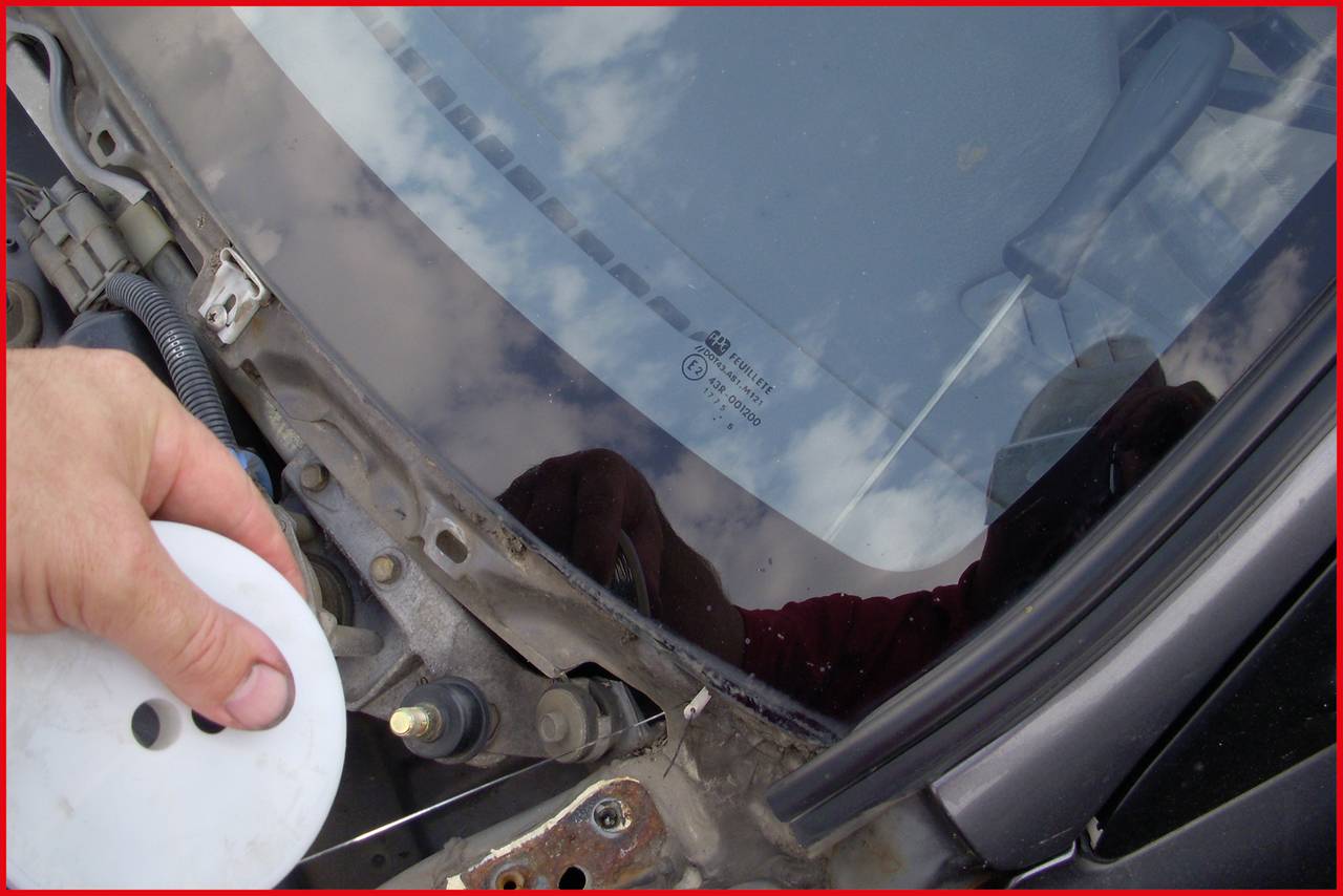 Zbliżenie osoby przygotowującej się do wyjęcia szyby samochodowej za pomocą rolki drutu. Samochód jest czarny.