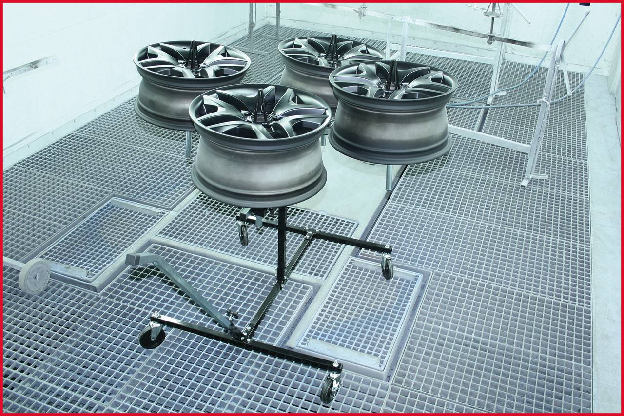 'Cztery lakierowane felgi samochodowe na stojaku w kabinie lakierniczej, gotowe do wysuszenia.'