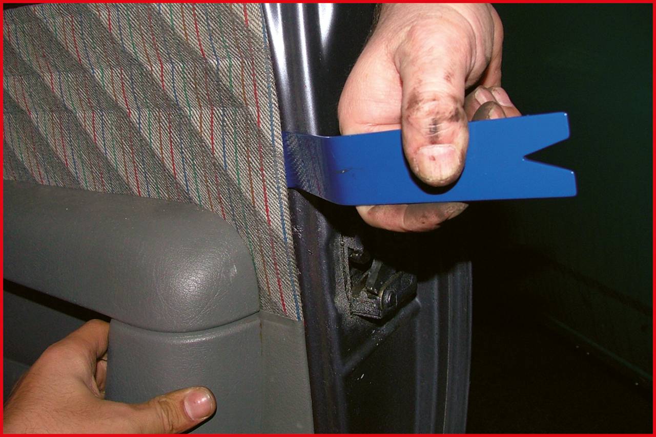 Osoba usuwa tapicerkę ramy drzwi samochodu za pomocą niebieskiego plastikowego narzędzia, aby dostać się do wewnętrznych części.