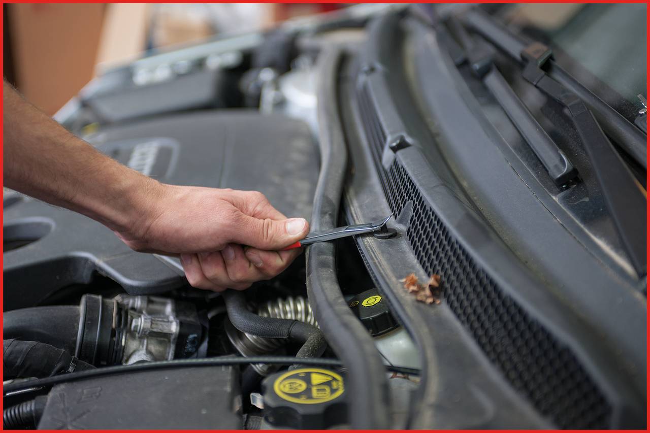 Dłoń naprawia komorę silnika samochodu za pomocą klucza. Fokus jest skierowany na konserwację silnika.