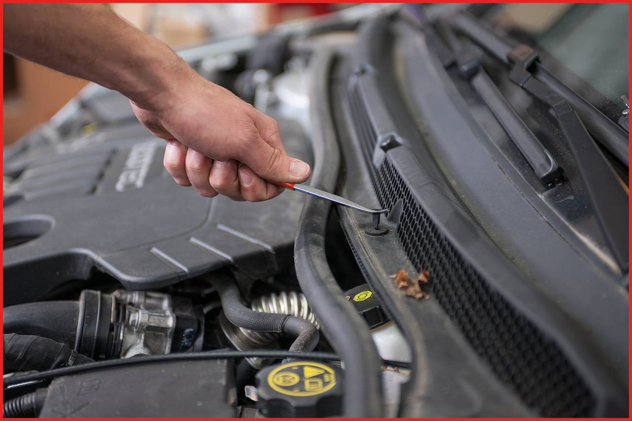 Ręka używa śrubokrętu do pracy przy masce samochodu.