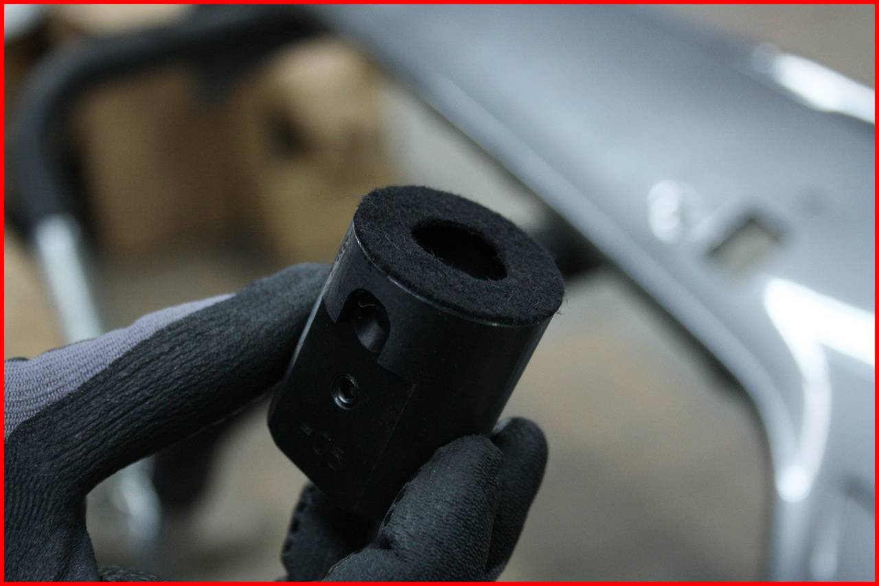 Jedna ręka trzyma małą, cylindryczną część metalową, która jest używana do celów mechanicznych lub technicznych. Na rozmytym tle widać kolejny metalowy przedmiot.