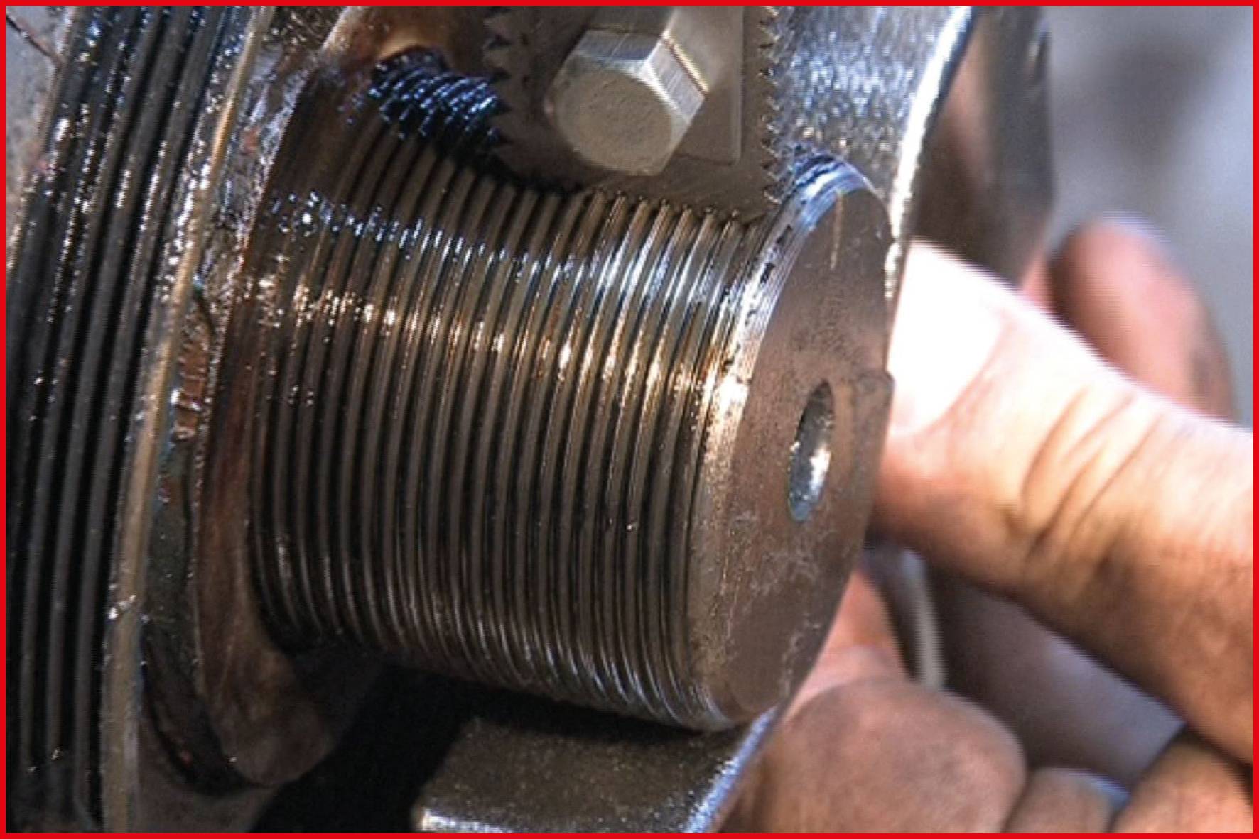 Zbliżenie elementu maszynowego z gwintem śruby. Ręka trzyma część, prawdopodobnie w celu przeprowadzenia inspekcji lub konserwacji.