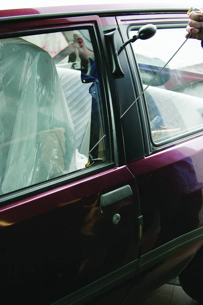 Osoba używa narzędzia, aby otworzyć drzwi burgundowego samochodu, prawdopodobnie podczas włamania lub w ramach pomocy drogowej.