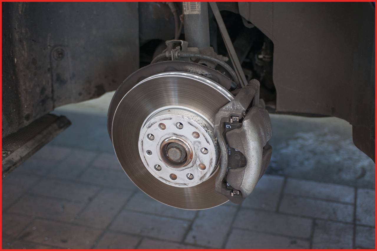Zbliżenie przedstawia układ hamulcowy samochodu ze składającymi się z tarczy hamulcowej i zacisku hamulcowego. Jest on rozmontowany i widoczny bez opony.