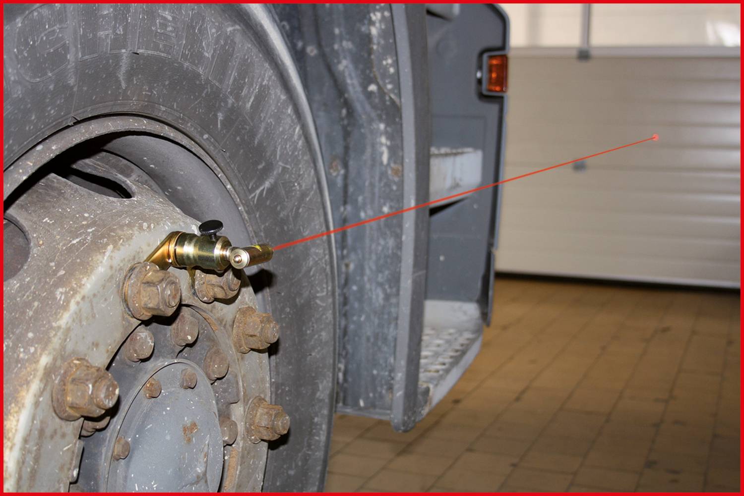 Koło ciężarówki z zamocowanym zaworem i dalmierzem laserowym skierowanym na odległy cel w środowisku warsztatu.