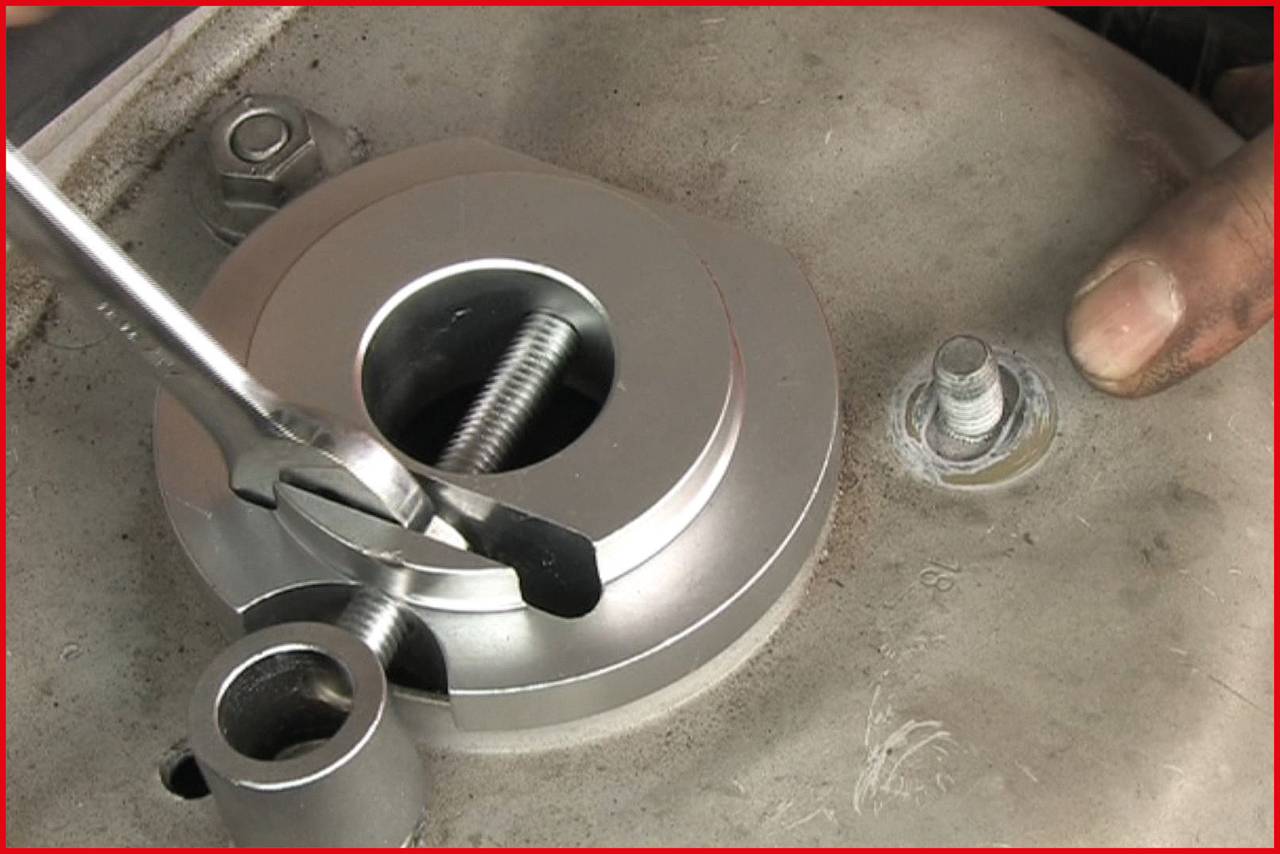 Jedna ręka trzyma klucz hydrauliczny, który jest przymocowany do dużej srebrnej nakrętki na metalowej płycie.