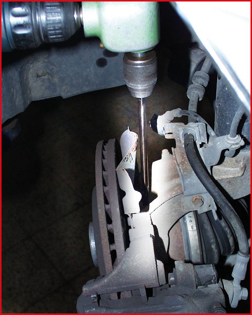 Zbliżenie narzędzia wiertniczego skierowanego na zardzewiałą tarczę hamulcową. Ostrość obrazu skupiona jest na precyzyjnym narzędziu.