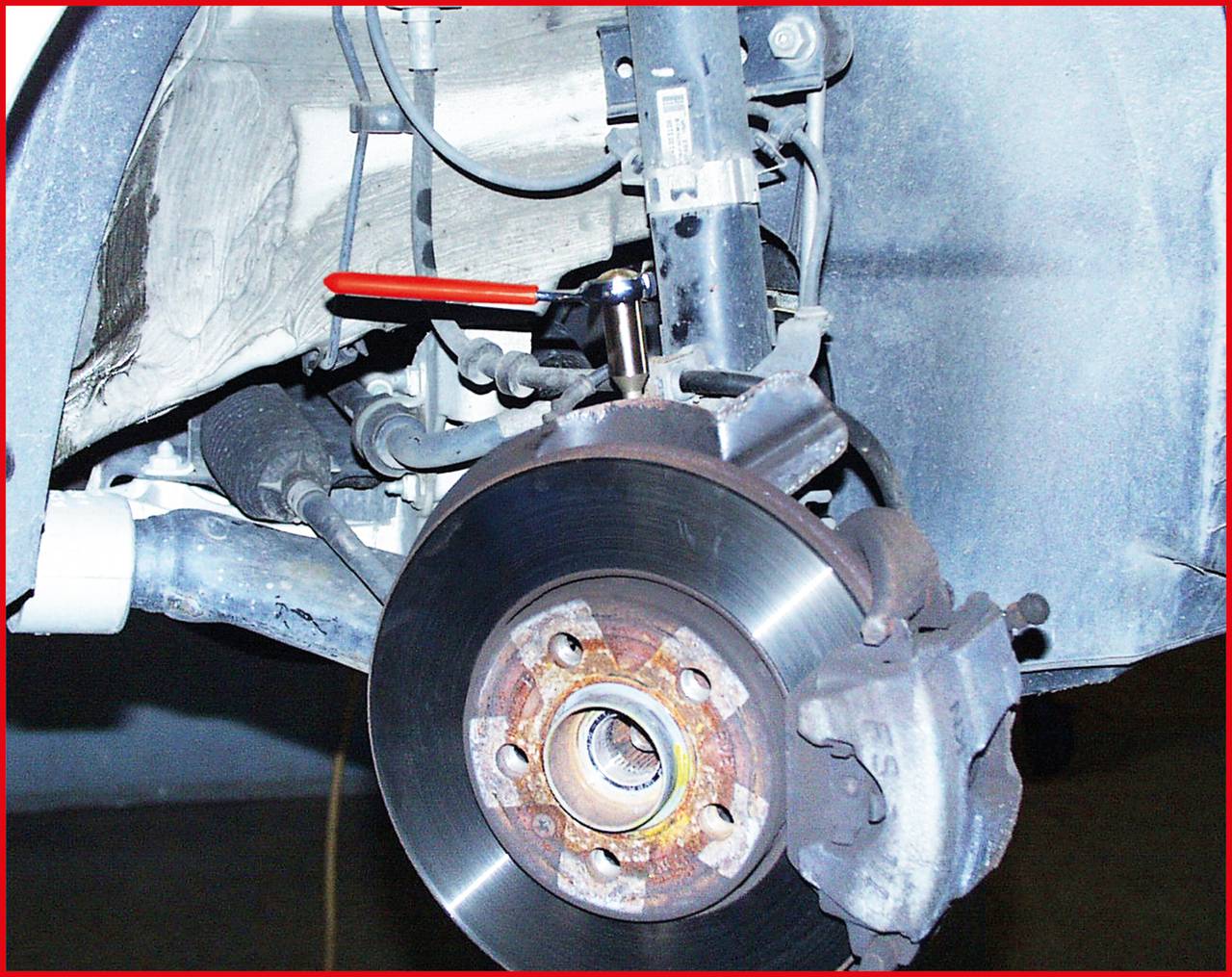 'Wbudowany system hamulcowy samochodu z widoczną tarczą i zaciskiem hamulcowym, częściowo rozłożony do naprawy lub czynności konserwacyjnych.'