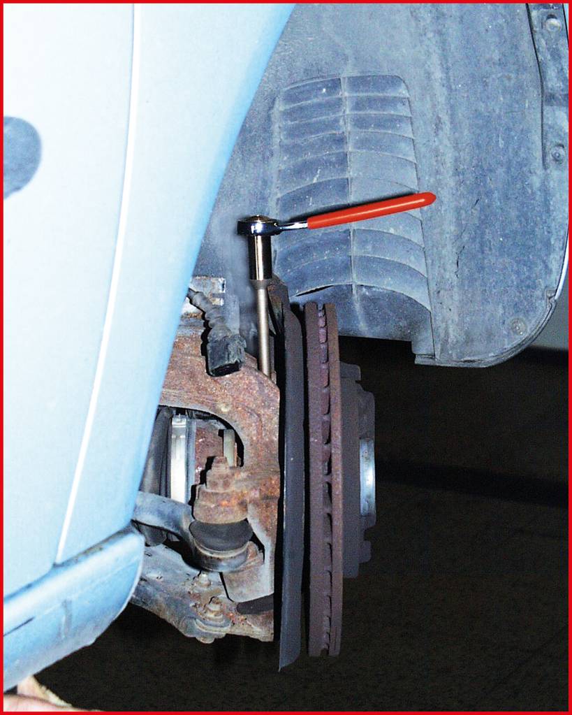 Zbliżenie demontowanego przedniego koła samochodu. Klucz z czerwonym uchwytem jest przymocowany do zacisku hamulcowego.