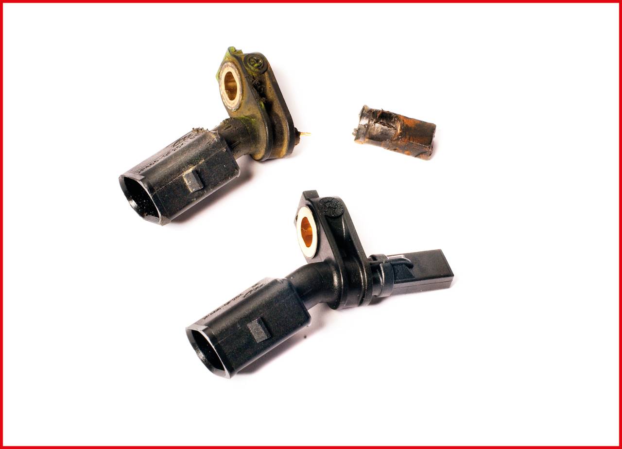 Dwa czujniki wału korbowego, jeden nowy i czarny, drugi stary i utleniony. Stary czujnik jest uszkodzony z odłamanym czubkiem.