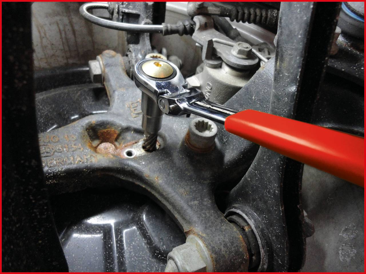 Ręka mechanika z czerwonym kluczem płaskim dokręca śrubę na zardzewiałej części w pomieszczeniu maszynowym. Użycie klucza dynamometrycznego.