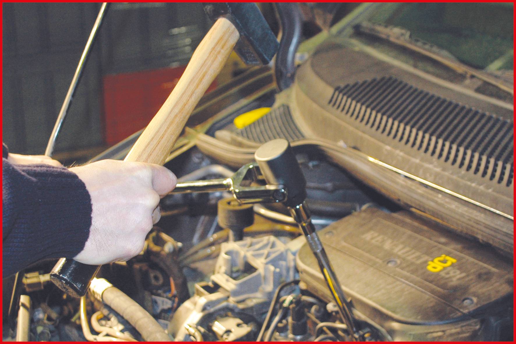 Osoba trzyma młotek nad otwartą komorą silnika pojazdu, jakby zamierzała przeprowadzić naprawę lub konserwację.