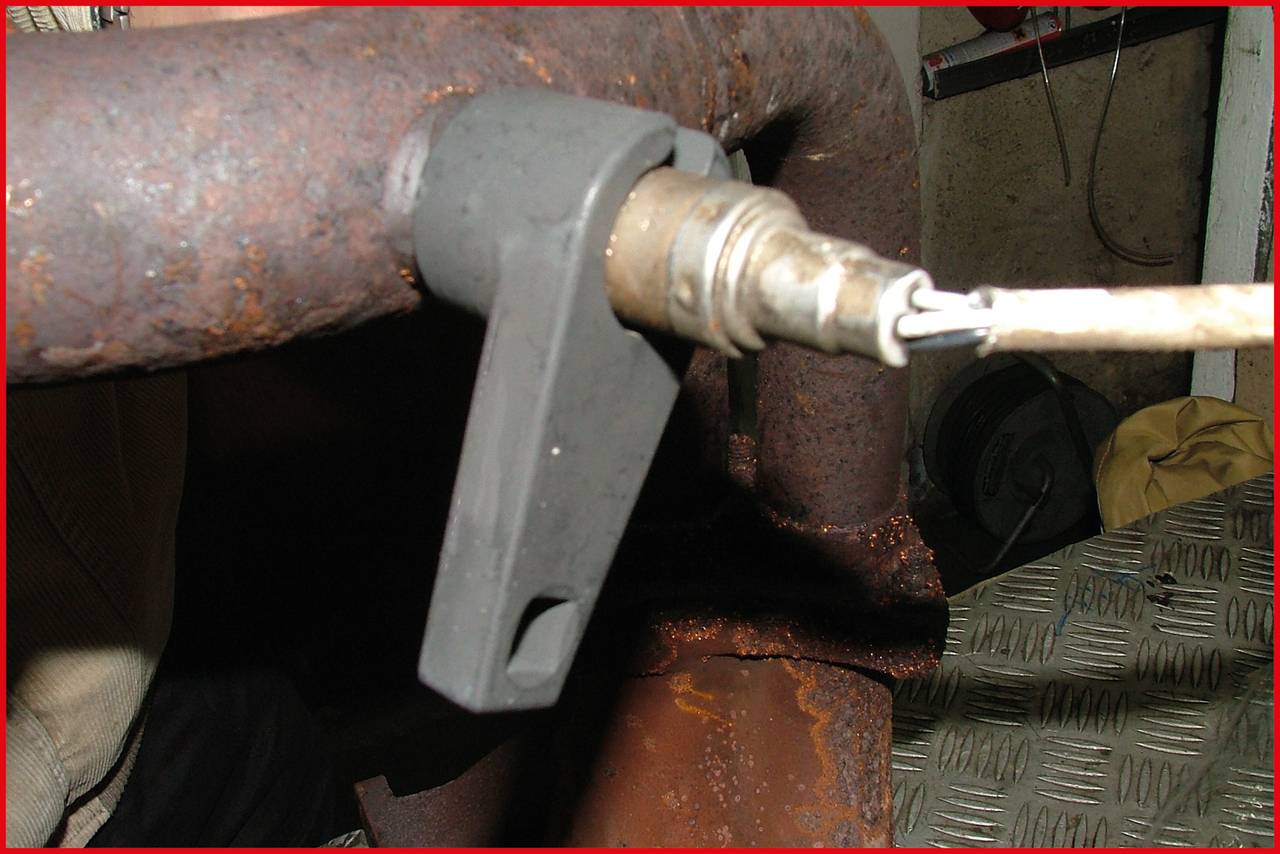 Zardzewiały przewód z zamontowanym czujnikiem, który wydaje się być częścią większego systemu maszynowego lub grzewczego.