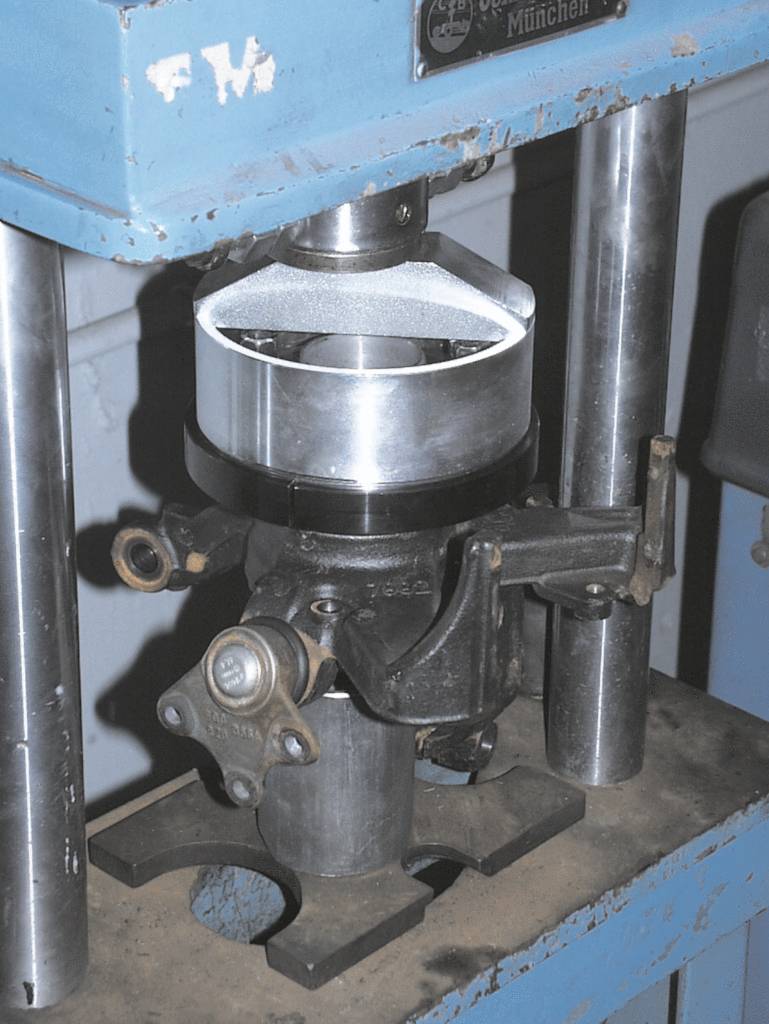 Maszyna do obróbki cylindrycznej części metalowej, zamocowanej między pionowymi podporami. Otoczenie przemysłowego warsztatu.