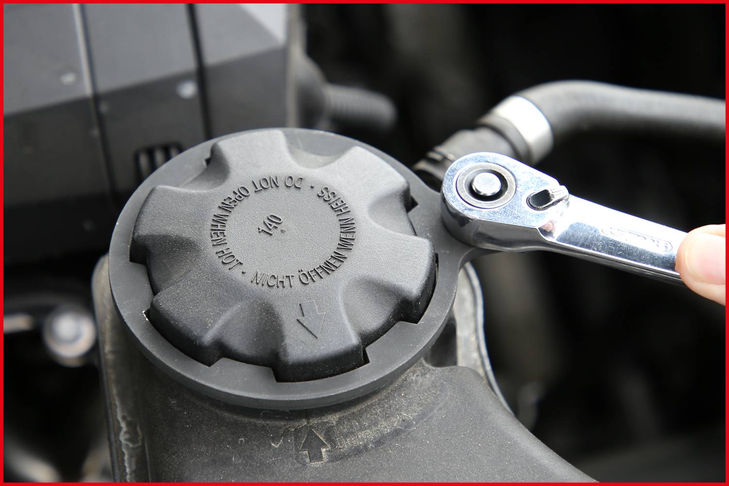 Klucz dokręcający jest przykładany do czarnej pokrywy oleju silnikowego. Tekst na pokrywie ostrzega, aby otwierać ją tylko przy wyłączonym silniku.