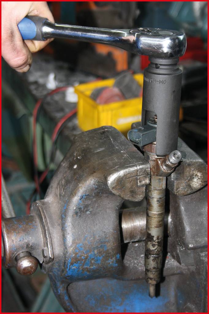 Osoba używa klucza dynamometrycznego, aby zamocować lub poluzować element w imadle. Na tle widoczne są narzędzia.