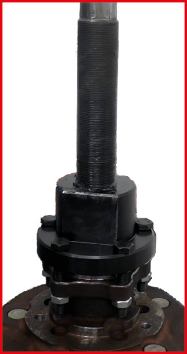 Czarna mechaniczna aparatura, prawdopodobnie zawór z wysokim gwintem śrubowym na górze, zamontowana na metalowej płycie.