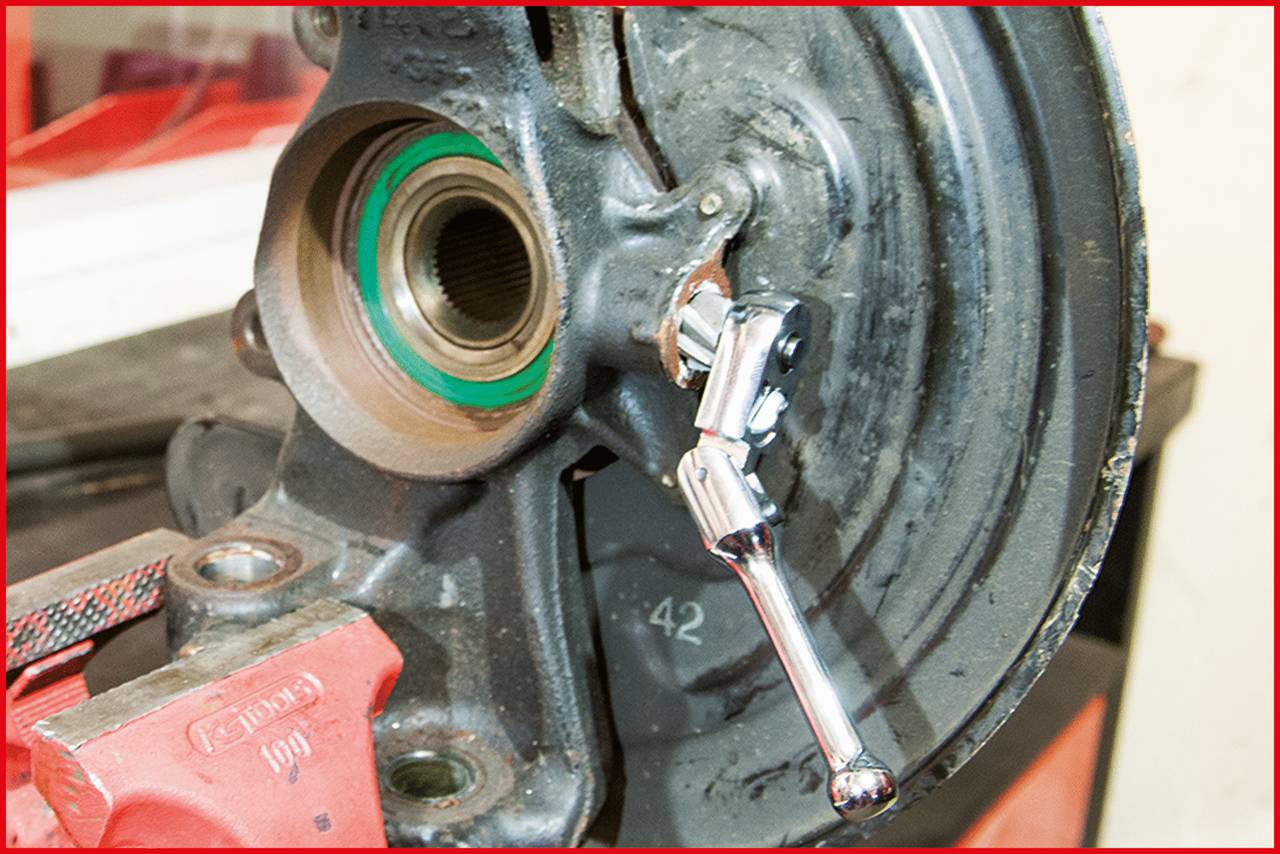 Zbliżenie komponenty części samochodowej z narzędziem umieszczonym na niej. Tło lekko rozmyte, fokus na mechanice.